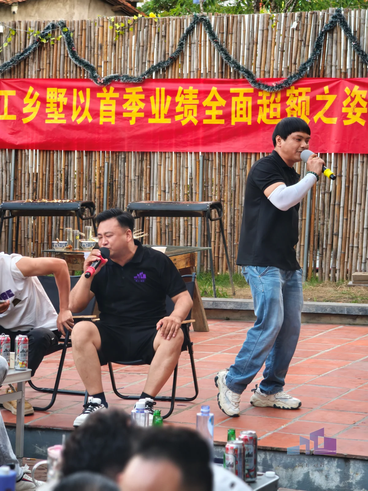 福建尚工乡墅装饰工程有限公司季度业绩庆祝活动现场，优秀男员工在横幅前手持麦克风登台发言。