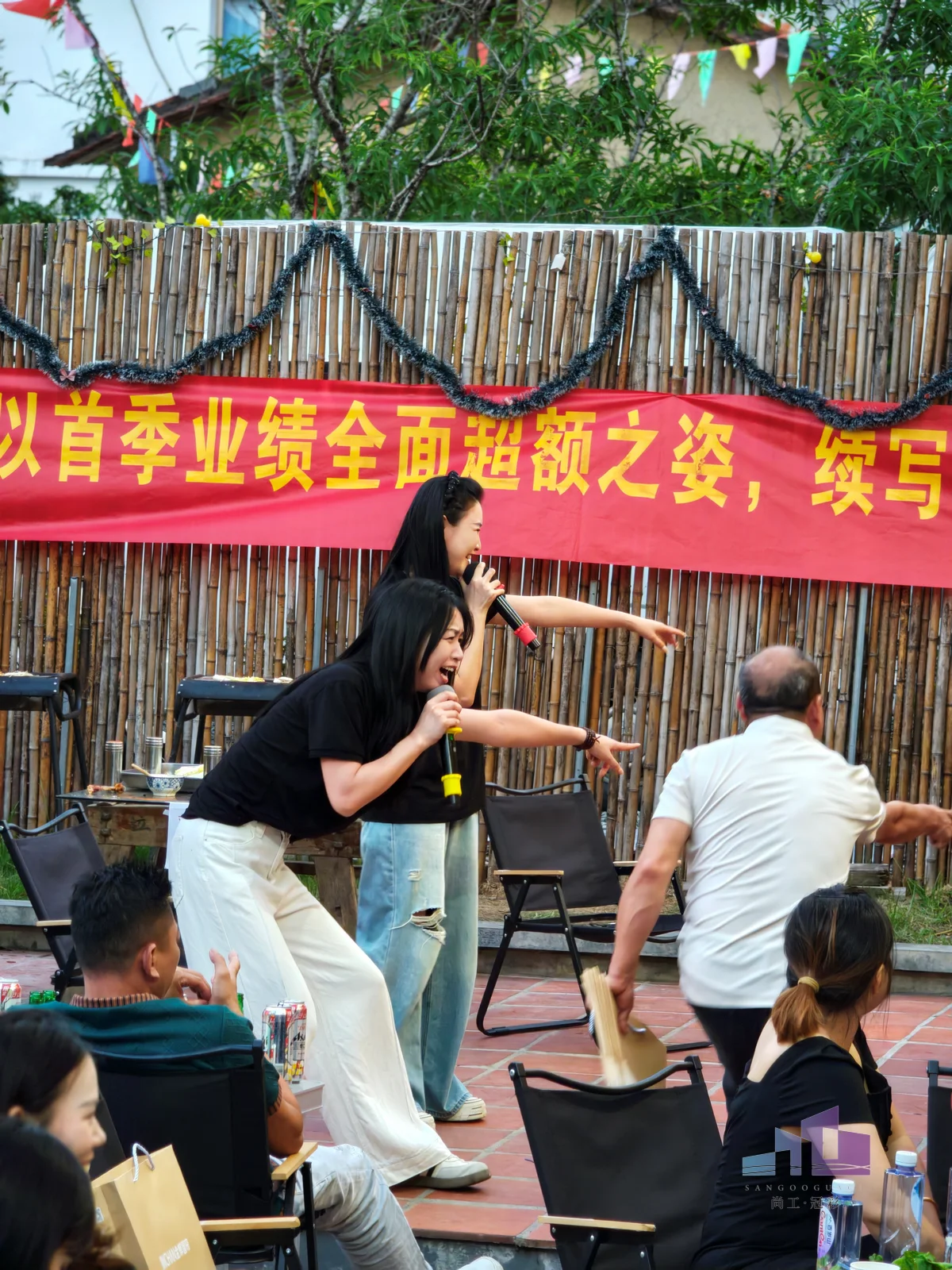 福建尚工乡墅装饰工程有限公司团队活动现场，两位富有活力的女员工手持麦克风热情主持并与台下互动。